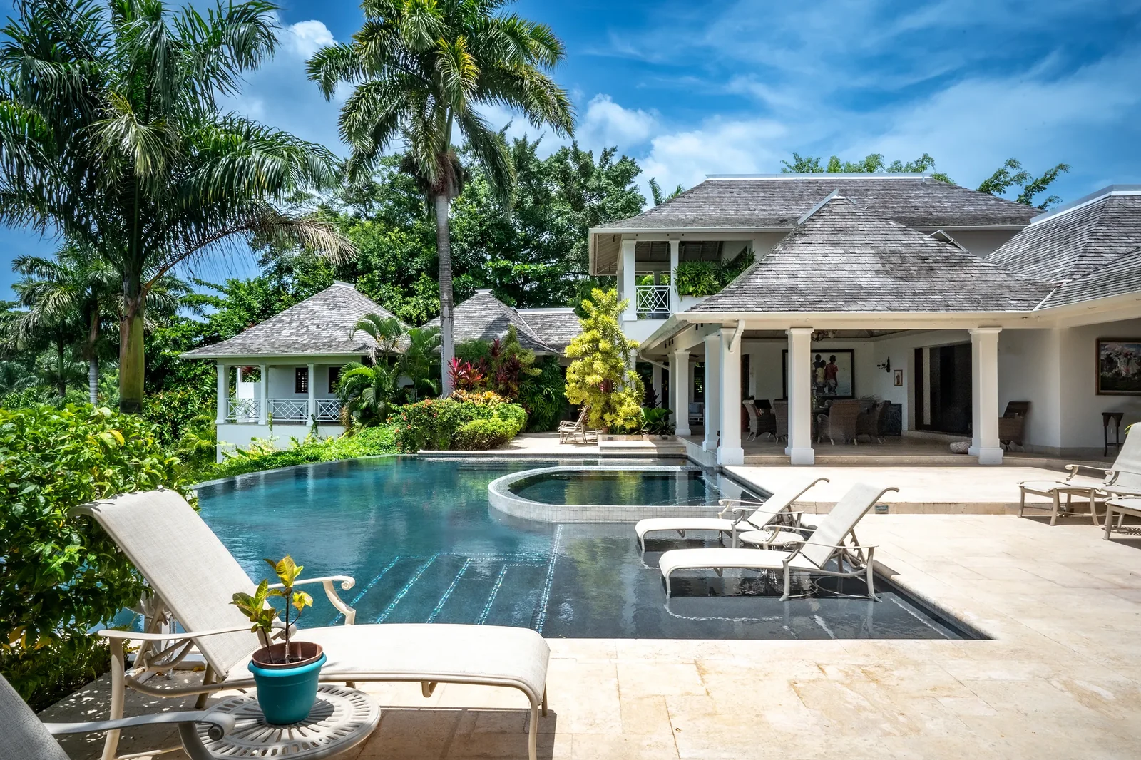A villa with infinity pool, loungers, and garden cottages